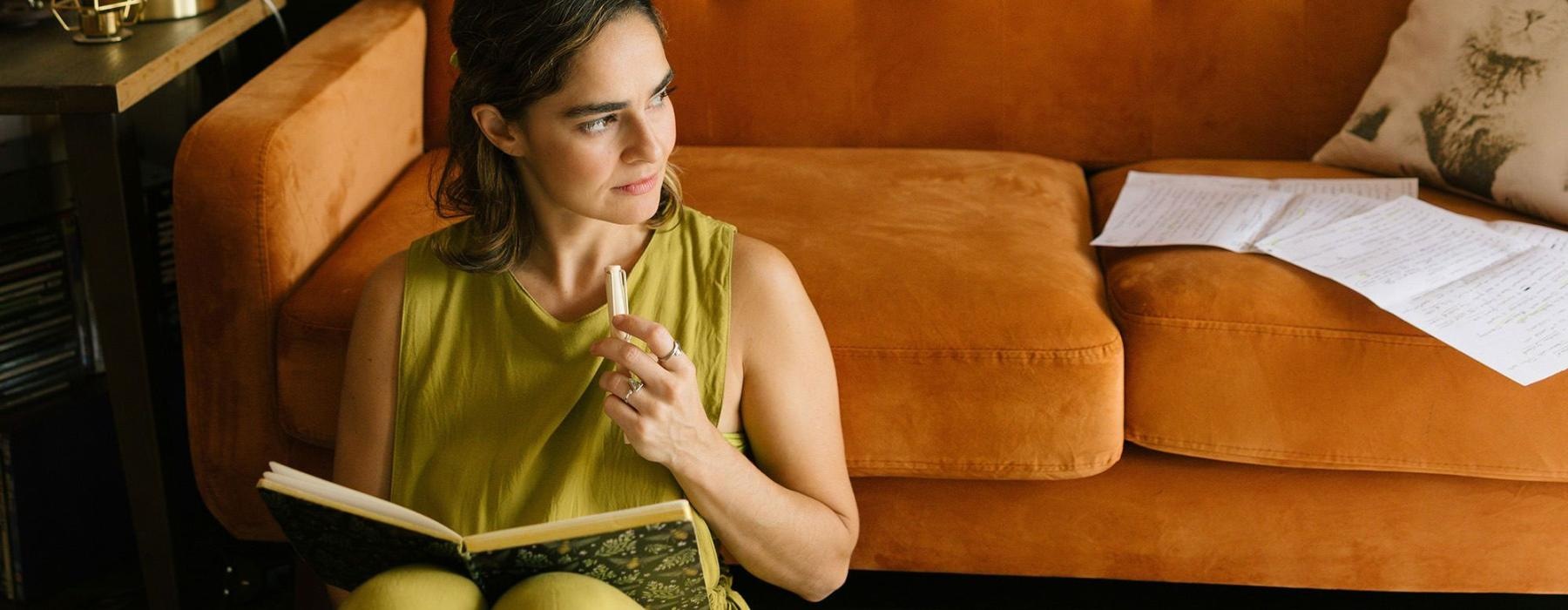 A woman sitting in front of a couch writing in a journal